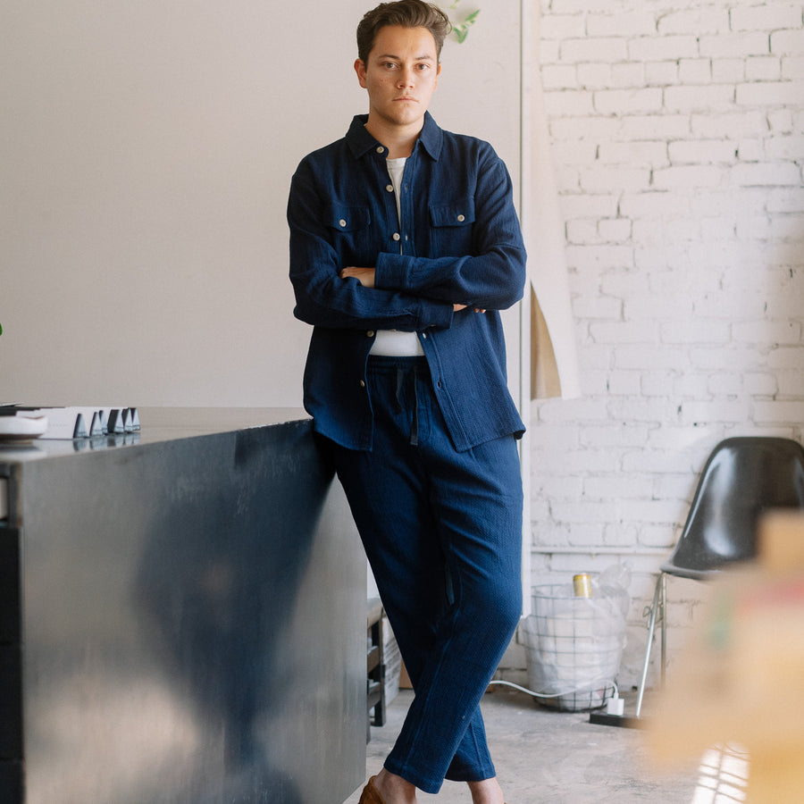 A man in a blue shirt and pants stands in a room.