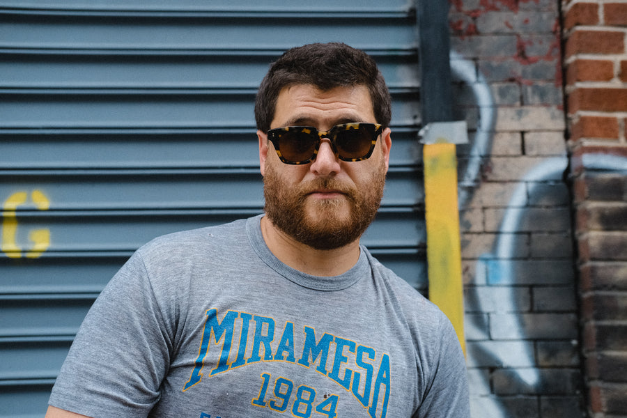 A portrait of a man in a grey tee and sunglasses 