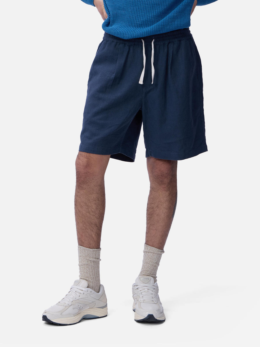 Person wearing navy shorts, a blue sweater, white sneakers, and gray socks on a white background