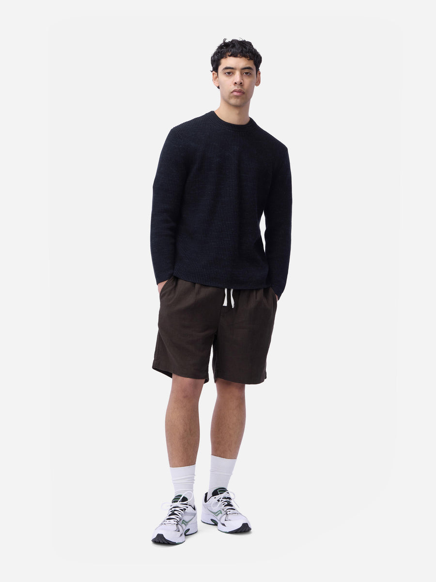 Man wearing a black long-sleeve shirt, brown shorts, and white sneakers on a white background