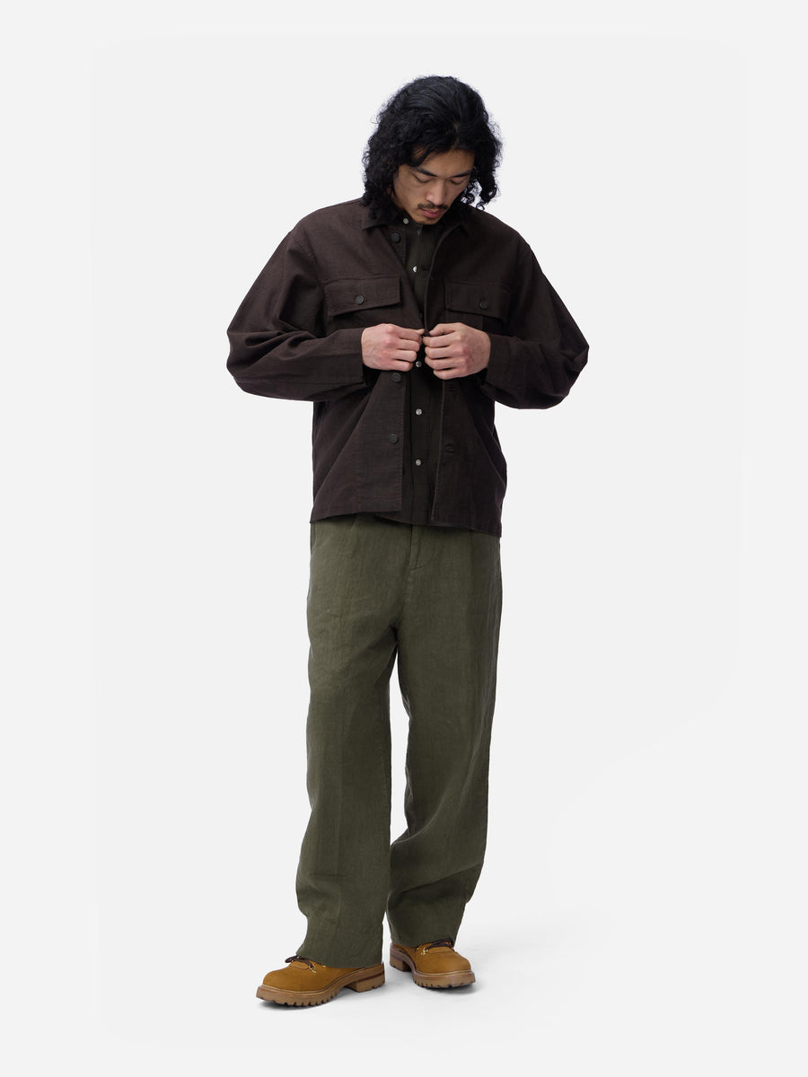 Person wearing a brown jacket and green pants on a white background