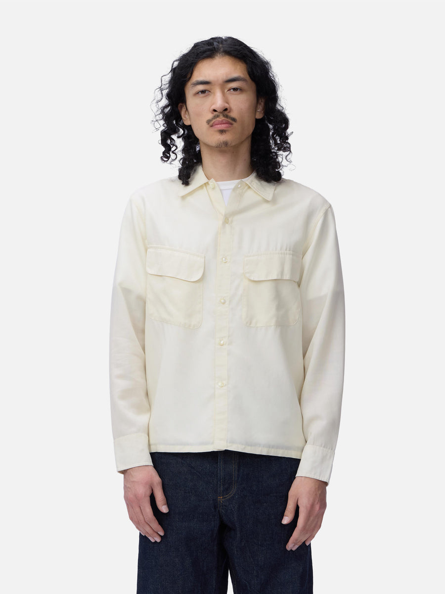 Man wearing a cream-colored button-up shirt with two front pockets on a white background