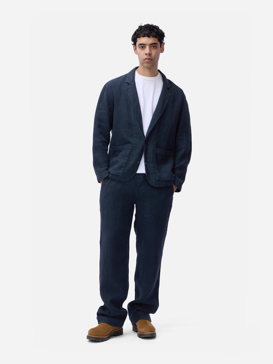 Man wearing a navy blazer, white shirt, and dark pants on a white background