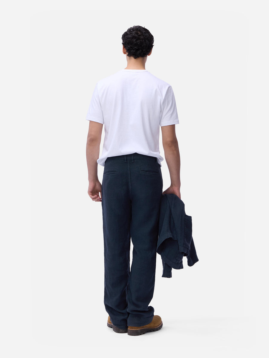 Person wearing a white t-shirt and dark pants holding a jacket on a plain background