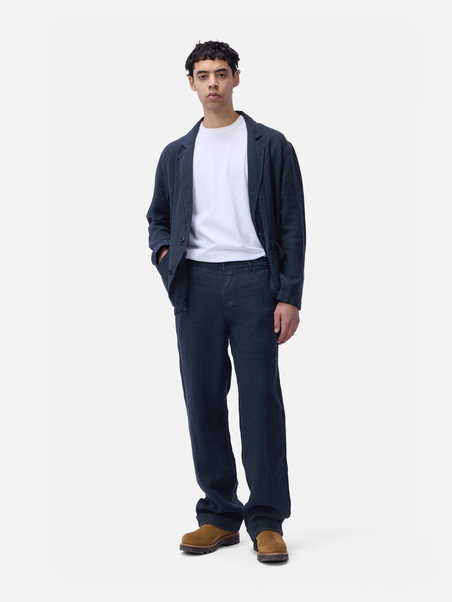Man wearing a navy cardigan, white shirt, dark pants, and brown shoes on a white background