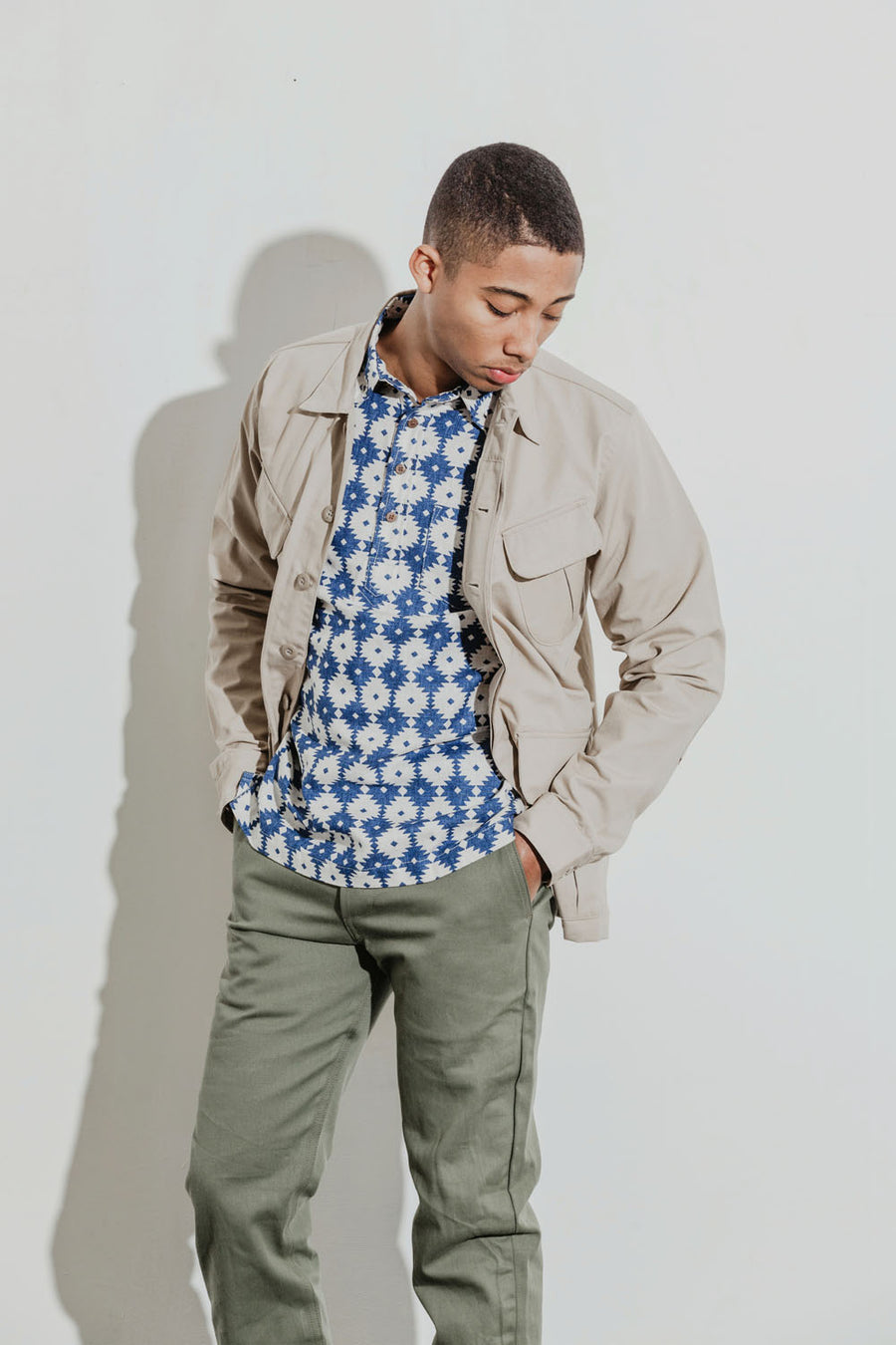 Model wears a blue aztec-patterned popover shirt under a khaki jacket.