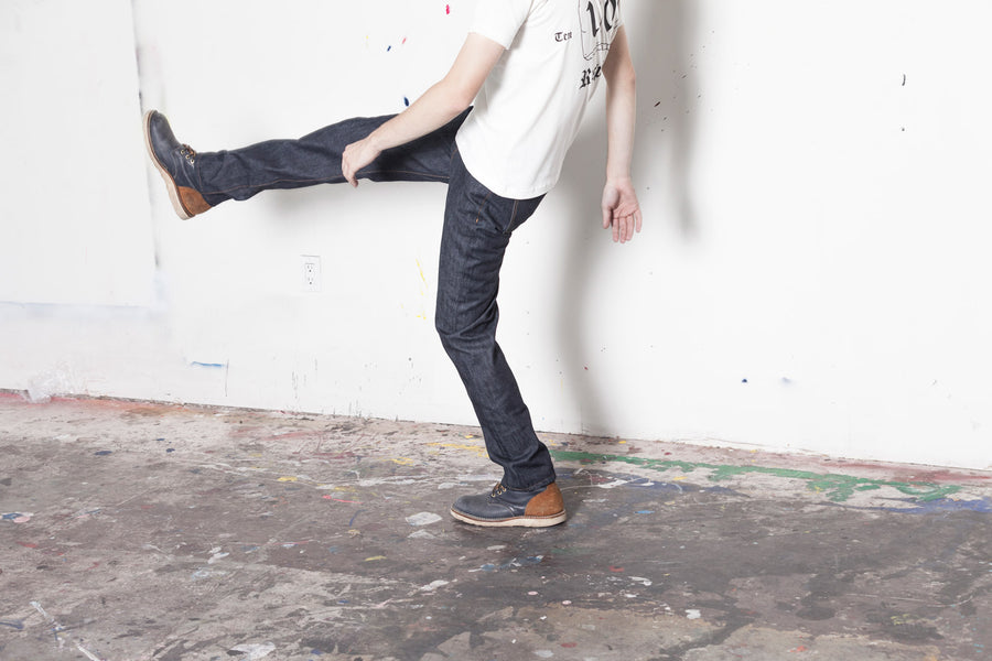 A model kicks his right leg out while wearing 3sixteen jeans.