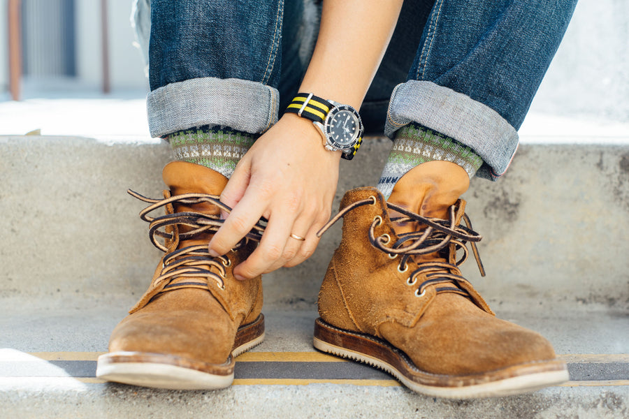 A closeup shot of blue jeans, green knit socks, and brown boots.