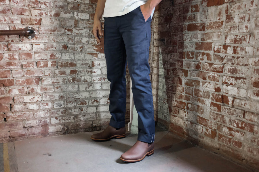 Model wearing the selvedge navy chinos in front of a brick wall